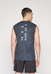 Crna majica bez rukava s uzorkom tie-dye, s bijelim natpisom "TRNG CLUB 24 7" vertikalno na leđima. Mat materijal, ležeran kroj.