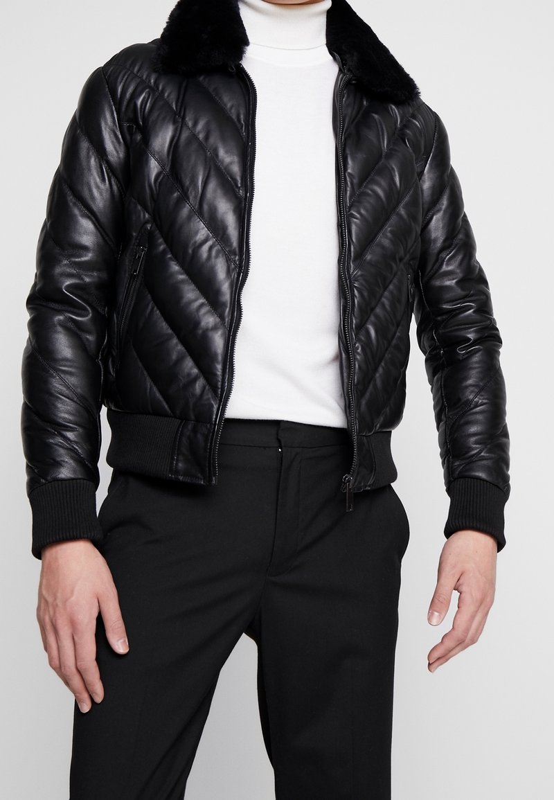 Černá kožená bomber bunda s prošívaným vzorem, měkkým límcem, žebrovanými manžetami a pasem, s předním zipem a bočními kapsami.
