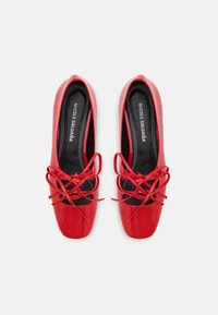 Red patent leather shoes with a square toe, featuring black lace accents and two narrow, crisscrossing laces on the front.