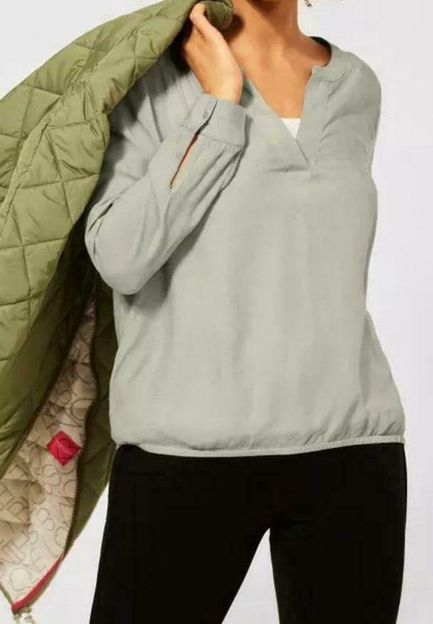 Pull-over gris clair avec un col en V, des manches longues et un ourlet élastique en bas. Veste matelassée vert olive avec un intérieur à motifs.