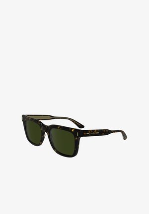 Lunettes de soleil à motif écaille de tortue avec verres verts, de forme carrée, et branches robustes. Présente un logo discret sur la branche.