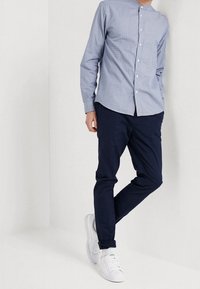 Lyseblå skjorte med knapper og et subtilt mønster, kombineret med mørkeblå chinos og hvide sneakers. Glat stof med en skræddersyet pasform.