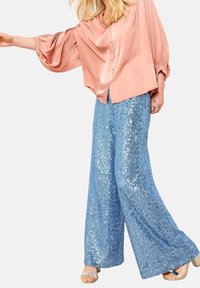 Pink satin blouse with puffed sleeves, paired with wide-leg blue sequined trousers and light-colored sandals. Shimmery texture on pants.