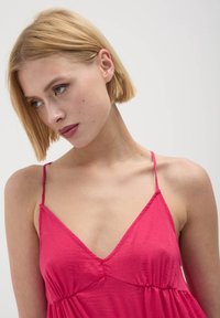 Abito senza maniche di un vivace rosa con scollatura a V profonda, vita arricciata e sottili spalline regolabili. Tessuto leggero con una consistenza liscia.