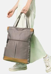 Grå tygväska med brunt botten och detaljer; har dubbel axelremmar och framficka med dragkedja; slät textur med strukturerad form.