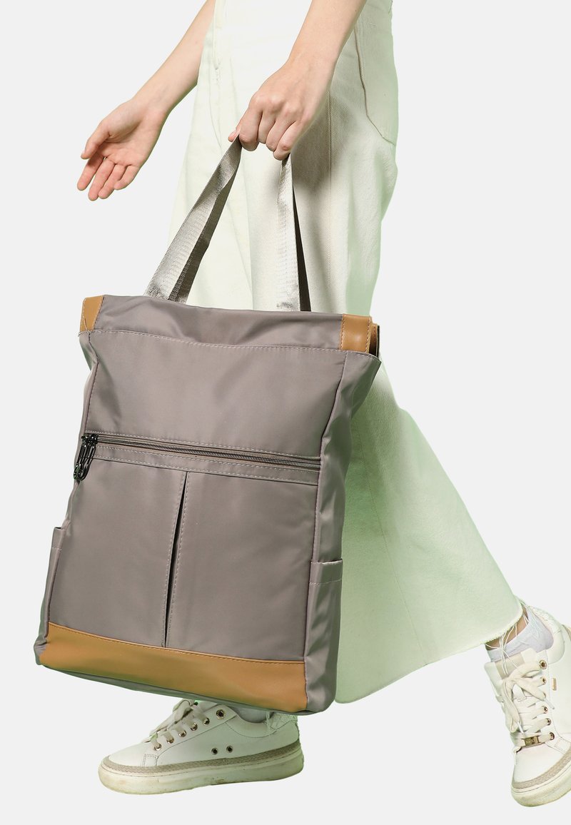 Grå tygväska med brunt botten och detaljer; har dubbel axelremmar och framficka med dragkedja; slät textur med strukturerad form.