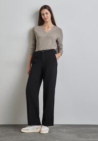 Beige v-ringad tröja med ribbade ärmslut, uppställd med högmidjade svarta byxor med en slät textur och framfickor, tillsammans med vita sneakers.