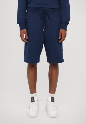 Mørkeblå sweatshorts laget av mykt materiale, med elastisk midjebånd og snøring, samt sidelommer og bukseben med oppbrett.