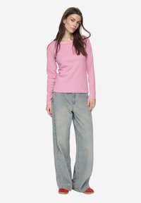 Langärmeliges roze top met lichtroze strepen, gecombineerd met losse, lichtblauwe denim spijkerbroek en rode schoenen, wat een casual stijl laat zien.