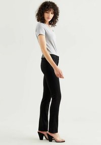 Top gris de manga corta y escote en V, jeans negros ajustados y sandalias de tacón bloque transparente. Tejido suave y silueta entallada, con detalles sutiles.
