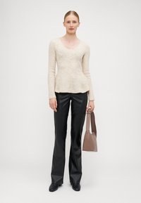 Bež pleteni longsleeve top s izrezom, uparen s crnim kožnim hlačama s našivenim nogavicama i taupe torbom s jednim remenom.