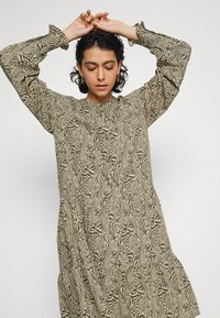 Vestido com padrão de zebra em tons terrosos. Mangas longas com punhos franzidos, decote redondo e saia em camadas para adicionar textura e fluidez.