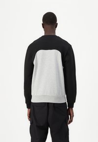 Felpa nera e grigia con pannello posteriore arrotondato. Polsini e orlo a costine. Realizzata in tessuto morbido, ideale per un look casual.