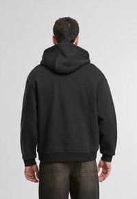 Svart huva med en stor, justerbar huva. Har ribbade ärmslut och fåll, avslappnad passform och mjuk tygtextur.