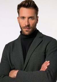 Blazer gris carbón con un acabado texturizado, bolsillo de pecho simple, combinado con un cuello de tortuga negro. Diseño formal, silueta ajustada.