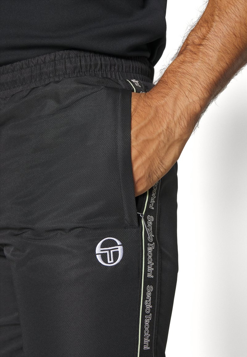 Jogging en polyester noir avec une finition texturée, incluant une poche latérale et un accent de logo blanc. Rayure sur le côté avec un détail de marque.