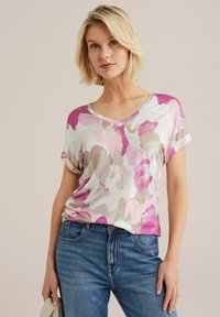 T-shirt s V-izrezom s cvjetnim uzorkom u ružičastim, ljubičastim i bež tonovima, izrađen od mekanog materijala. Rukavi su savijeni, a kroj je opušten.