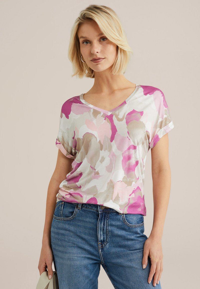 T-shirt s V-izrezom s cvjetnim uzorkom u ružičastim, ljubičastim i bež tonovima, izrađen od mekanog materijala. Rukavi su savijeni, a kroj je opušten.