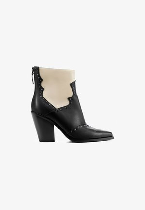 Černobéžová kotníková bota s špičatou špičkou, blokovým podpatkem, ozdobnými stříbrnými nýty a zipem na zadní straně.