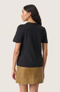 Tricou negru cu mânecă scurtă și guler rotund. Asortat cu o fustă din piele bej, având o textură netedă și o siluetă simplă.