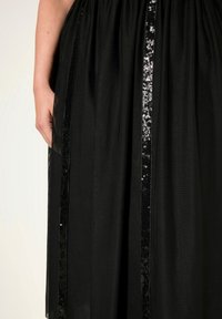 Abito nero con vita arricciata, tessuto trasparente e dettagli a strisce di paillettes sul davanti, creando un aspetto testurizzato e a strati.
