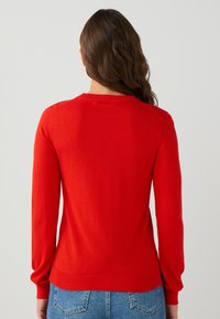Pull rouge à manches longues, avec un col rond et des bords côtes aux poignets et à l'ourlet. Fabriqué en tissu doux et léger avec une texture lisse.