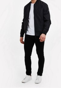 Cazadora bomber negra con cremallera frontal y dobladillo acanalado, combinada con una camiseta blanca, jeans skinny negros y zapatillas blancas.