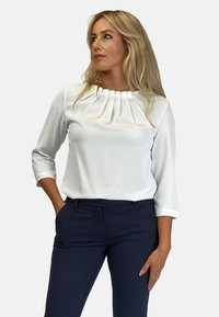 Biała bluzka z rękawami trzyczwartkowymi z plisowanym dekoltem. Połączona z granatowymi spodniami w wzorki. Gładka tekstura, dopasowany krój.