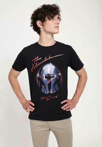 Svart bomull T-shirt med en grafisk bild av en hjälm från "The Mandalorian." Texten lyder "The Mandalorian" och "This is the way."
