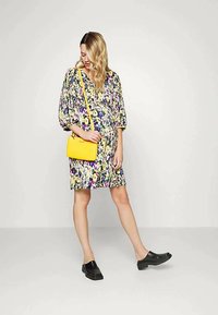Vestido floral com mangas bufantes em amarelo, azul, rosa e verde. Combinado com uma bolsa transversal amarela brilhante e tamancos pretos.