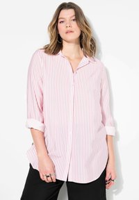 Camisa de botones rosa claro con finas rayas verticales rojas, mangas enrolladas y un dobladillo curvado. La tela parece suave y ligera.