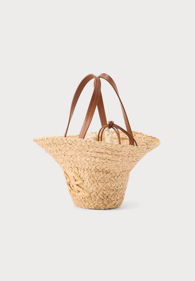 Πλεκτή τσάντα από ψάθα με φαρδιά ύφανση σώματος, δερμάτινες λαβές και εσωτερική υφασμάτινη θήκη με κορδόνι, πάνω σε απλό φόντο.