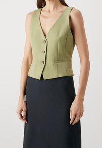 Grön, ärmlös väst med djup V-ringning, fem knappar och två sidofickor. Tyget verkar ha en texturerad yta, med en strukturerad och åtsittande design.