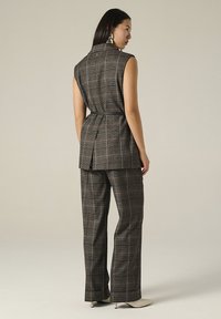 Gilet à carreaux gris et pantalon assorti avec une taille ceinturée, en tissu texturé. Comprend des accents subtils de marron clair.