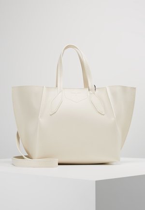 Bolso tote de cuero color crema con dos asas, paneles laterales extendidos y una correa de hombro desmontable sobre un pedestal blanco.