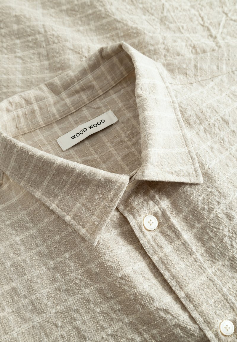 Chemise beige texturée avec un motif à carreaux. Présente un col classique et des boutons blancs. L'étiquette indique "WOOD WOOD."