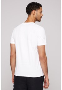 Camiseta blanca de manga corta hecha de tela suave, con cuello redondo y un corte holgado. Las costuras visibles a lo largo de los bordes añaden detalle.