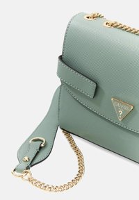 Grüne Handtasche aus strukturiertem Kunstleder mit goldenem Kettenriemen, versehen mit einem dreieckigen Logo und einer Klappe mit kontrastierendem schwarzem Rand.