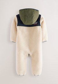 Mono de forro polar color crema con capucha verde y panel de hombros en azul marino. Presenta una textura acolchada y cierre frontal con cremallera. Logo de la marca visible.