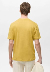 Kortærmet gul bomulds T-shirt, afslappet pasform, glat tekstur, simpel rund halsudskæring, vist fra ryggen med synlige syninger.