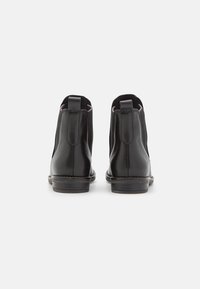 Ein Paar schwarze Leder-Stiefeletten mit niedrigen gestapelten Absätzen, elastischen Seiteneinsätzen und Zuglaschen, von hinten auf einem weißen Hintergrund gesehen.