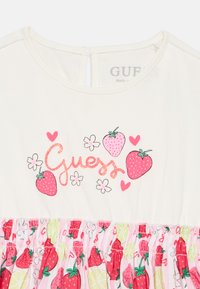 Λευκό βαμβακερό φόρεμα με ροζ λογότυπο "Guess" και γραφικές φράουλες, με σούρα στο κάτω μέρος σε φρουτένιο σχέδιο.