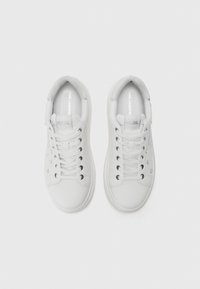 Adidași albi cu un superior din textil neted, vârf rotunjit, șireturi în față și detalii argintii ale logo-ului pe limbă și pe lateral.