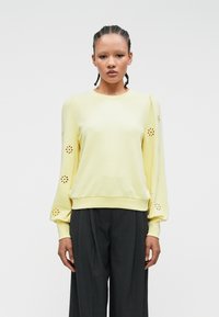 Gul sweatshirt med puffete ermer som har blomsterutskjæringer ved mansjettene. Mykt stoff og tilpasset nederkant med en avslappet design.