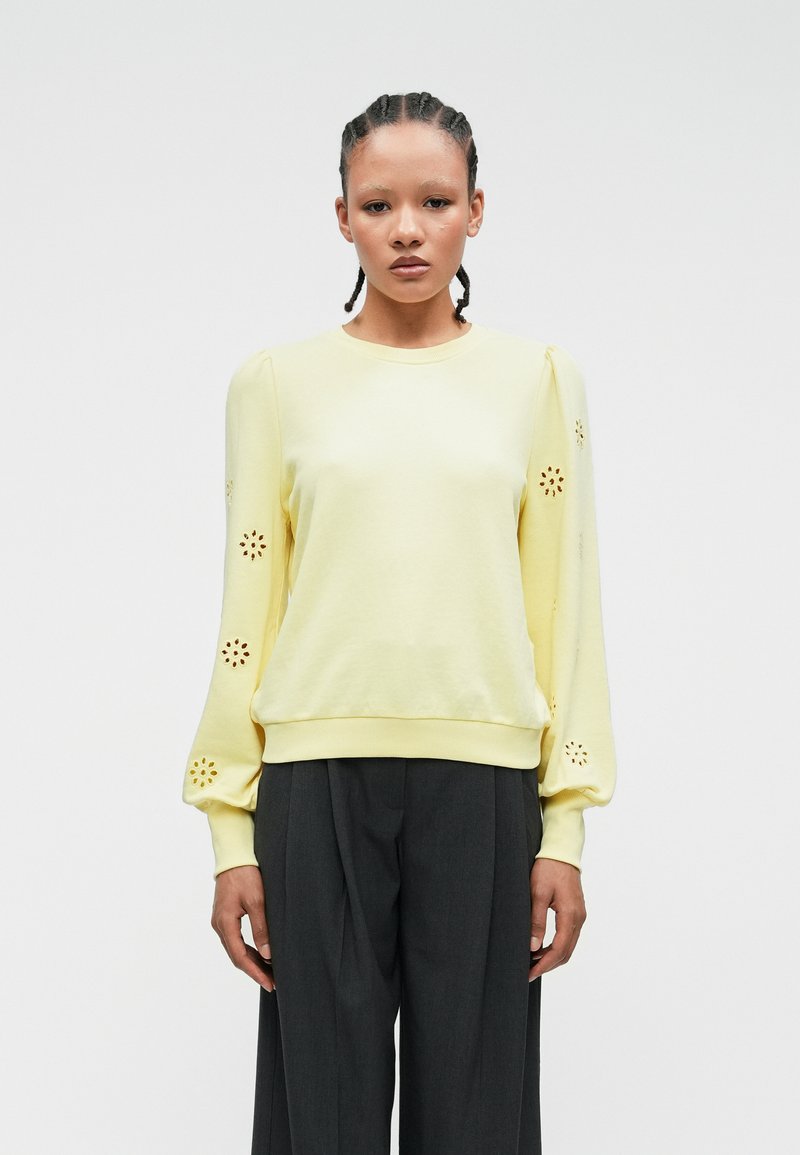 Gul sweatshirt med puffete ermer som har blomsterutskjæringer ved mansjettene. Mykt stoff og tilpasset nederkant med en avslappet design.