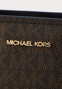 Hnedá textúrovaná materiál s zlatým logom "MICHAEL KORS". Obsahuje jemný vzor a hladké okraje, čím zdôrazňuje bohatú farbu a dizajn.