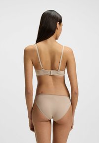 Beige rintaliivi- ja alushoususetti, joka on valmistettu sileästä kankaasta. Setissä on säädettävät hihnat, pitsipaneeli takana ja saumattomat reunat mukavuutta varten.