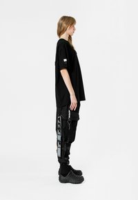Camiseta negra de gran tamaño, de material de algodón, combinada con pantalones cargo negros con bolsillos y acentos gráficos. Calzado: zuecos negros texturizados.