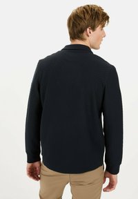 Navy quilted long-sleeve polo shirt with a textured surface and collar, paired with light beige pants. Focus on back view and structured fit.