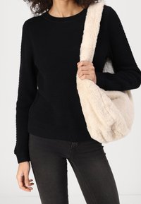 Czarny sweter z fakturowanego dzianiny z prążkowanym dekoltem, w połączeniu z miękką kremową torbą na ramię z sztucznego futra. Model nosi ciemne dżinsy.